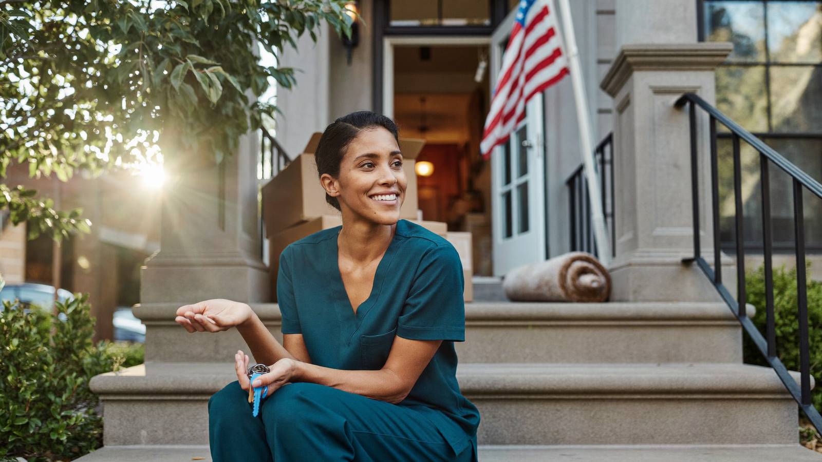 A nurse sits on greystone front steps in morning light, house keys resting in her palm.