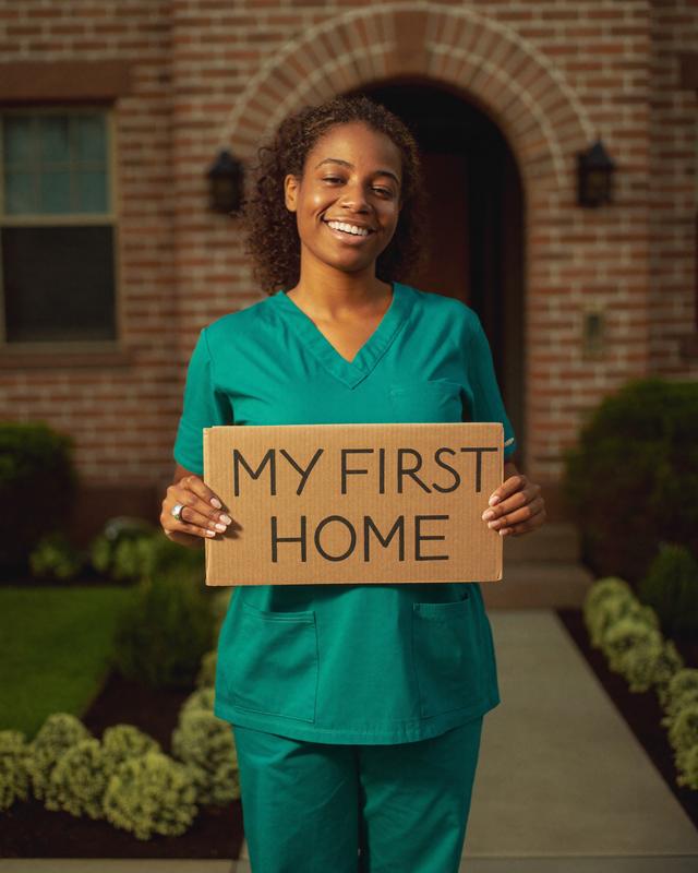 A nurse holds a cardboard sign reading MY FIRST HOME under the brick arch of a Chicago bungalow.